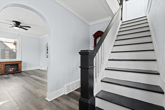 staircase with arched walkways, ornamental molding, wood finished floors, and visible vents