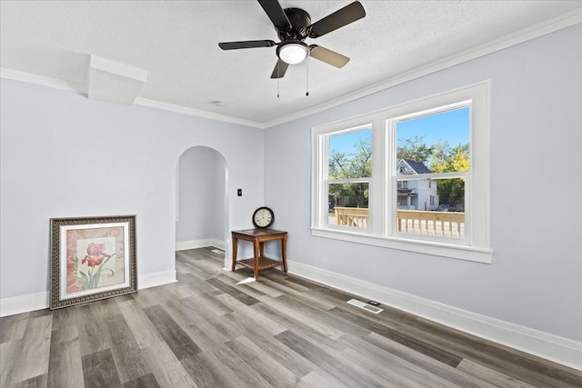 empty room with arched walkways, a textured ceiling, wood finished floors, baseboards, and ornamental molding