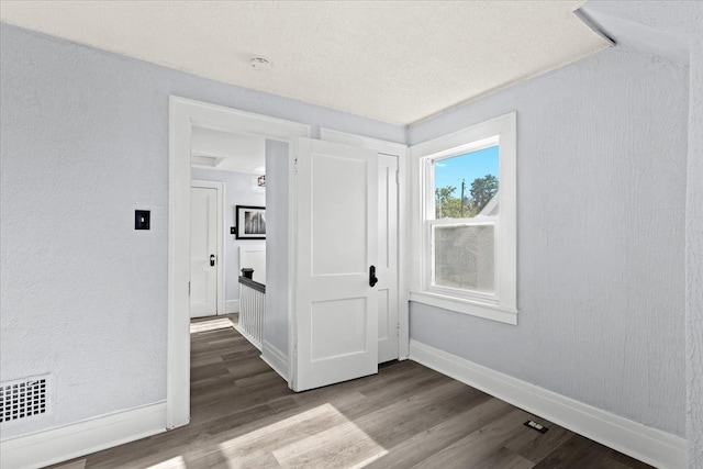 spare room featuring baseboards, visible vents, wood finished floors, and a textured wall