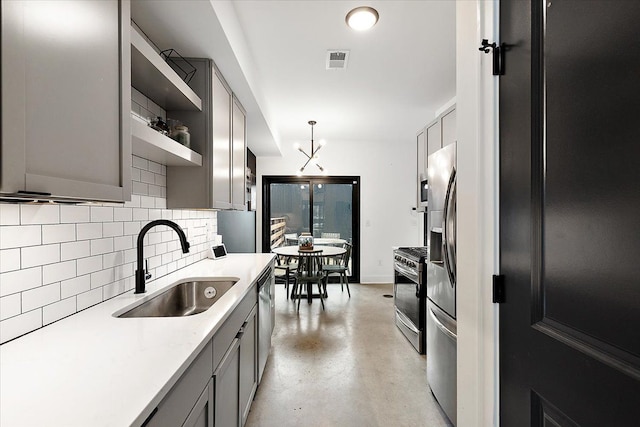 kitchen featuring stainless steel appliances, tasteful backsplash, gray cabinetry, a sink, and concrete flooring