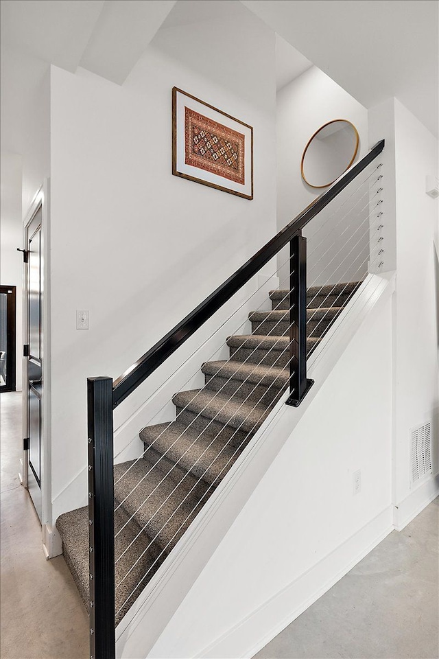 staircase featuring finished concrete flooring, baseboards, and visible vents