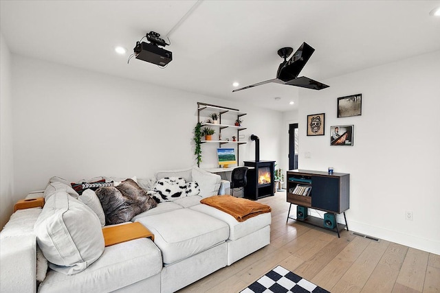 living room with recessed lighting, visible vents, light wood-style flooring, a wood stove, and baseboards