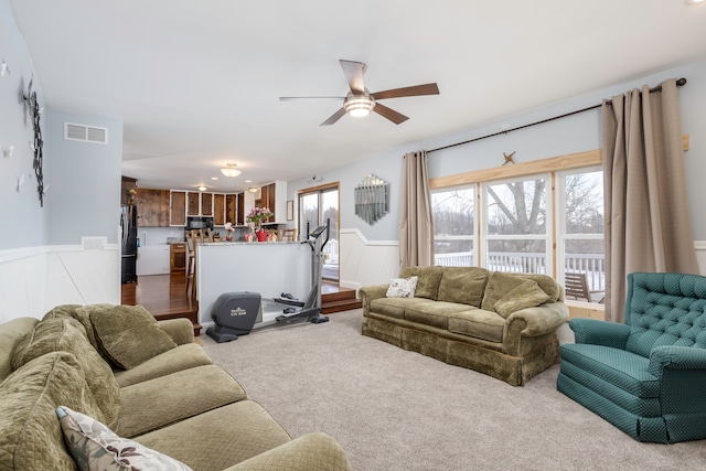 living room featuring ceiling fan, visible vents, dark colored carpet, and wainscoting