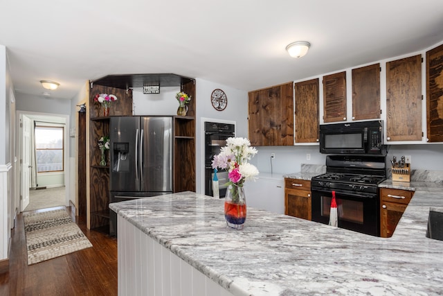 kitchen with light stone countertops, black appliances, a peninsula, and dark wood finished floors