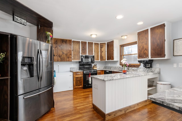 kitchen with wood finished floors, a peninsula, light stone countertops, black appliances, and recessed lighting