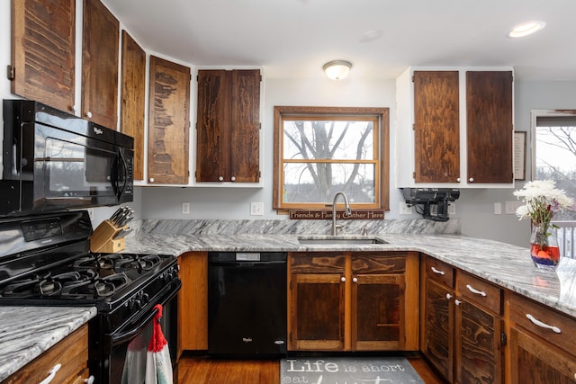 kitchen with light stone countertops, black appliances, a wealth of natural light, and a sink