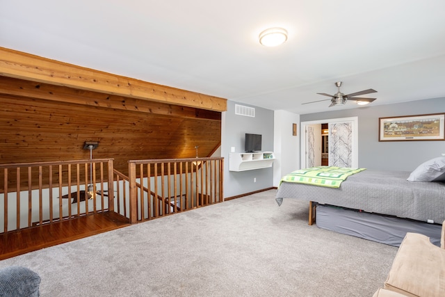 carpeted bedroom featuring visible vents, ceiling fan, wooden walls, and baseboards