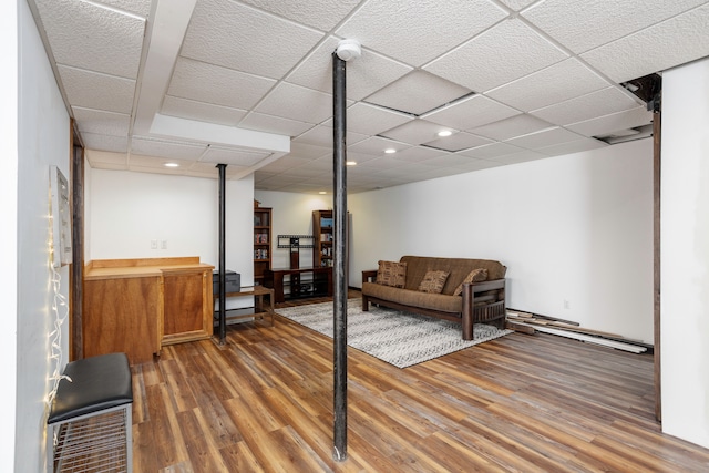 finished below grade area featuring a baseboard radiator, wood finished floors, and a paneled ceiling