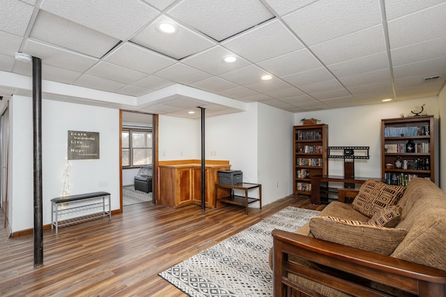 living room with a drop ceiling, recessed lighting, wood finished floors, baseboards, and a wood stove