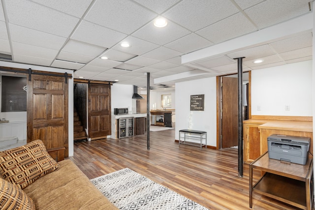 living room with a barn door, a ceiling fan, wood finished floors, a paneled ceiling, and recessed lighting