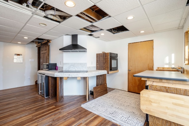 kitchen featuring recessed lighting, wall chimney range hood, black appliances, and wood finished floors