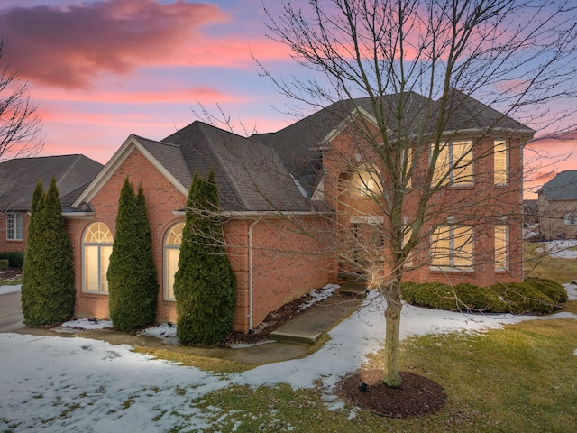 view of snow covered exterior with brick siding and roof with shingles