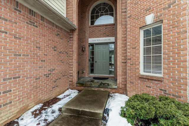 snow covered property entrance featuring brick siding