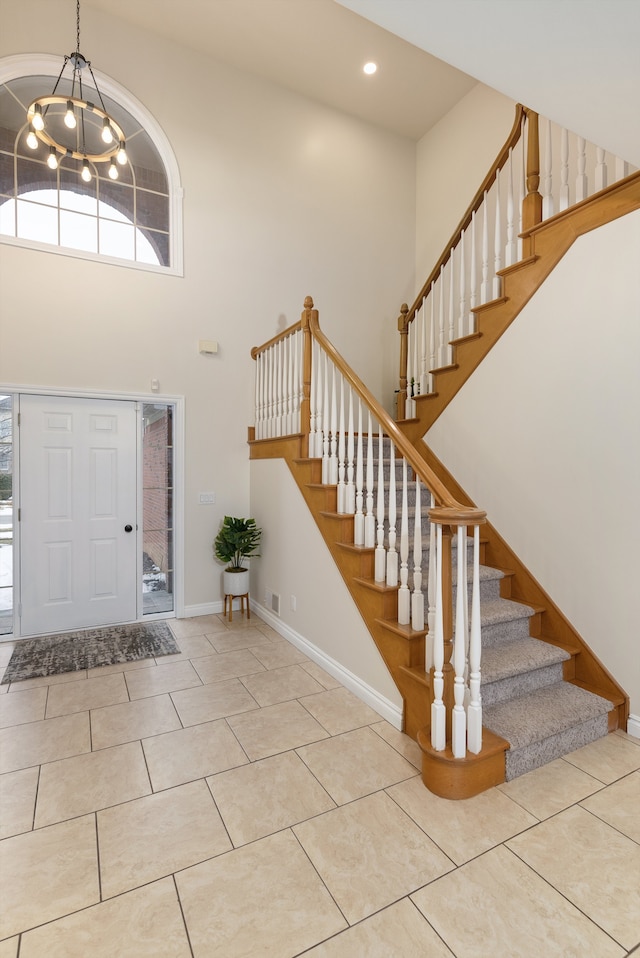 foyer entrance featuring a towering ceiling, tile patterned flooring, baseboards, and a chandelier