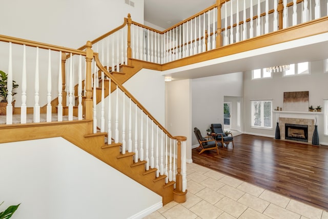 staircase with visible vents, a high ceiling, wood finished floors, a tile fireplace, and baseboards