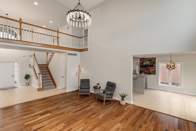 living area featuring a notable chandelier, wood finished floors, a towering ceiling, baseboards, and stairs