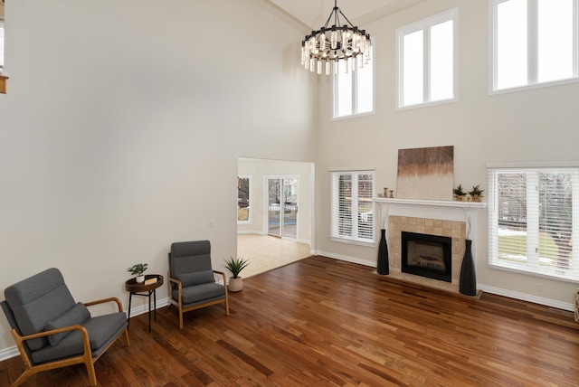 sitting room with baseboards, a tiled fireplace, wood finished floors, and a notable chandelier