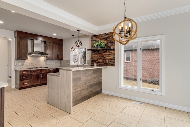 kitchen featuring dark brown cabinetry, visible vents, a peninsula, wall chimney range hood, and backsplash