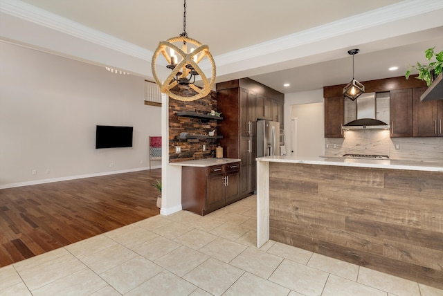 kitchen featuring light countertops, wall chimney range hood, dark brown cabinets, tasteful backsplash, and crown molding