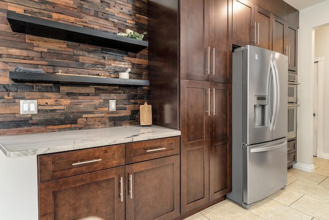 kitchen with light tile patterned floors, open shelves, backsplash, light stone countertops, and stainless steel fridge