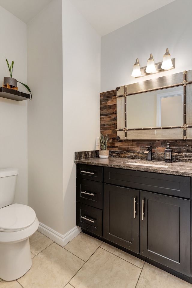 half bathroom with toilet, tile patterned floors, baseboards, and vanity