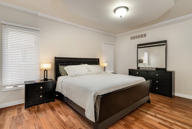 bedroom featuring baseboards, visible vents, wood finished floors, crown molding, and multiple windows