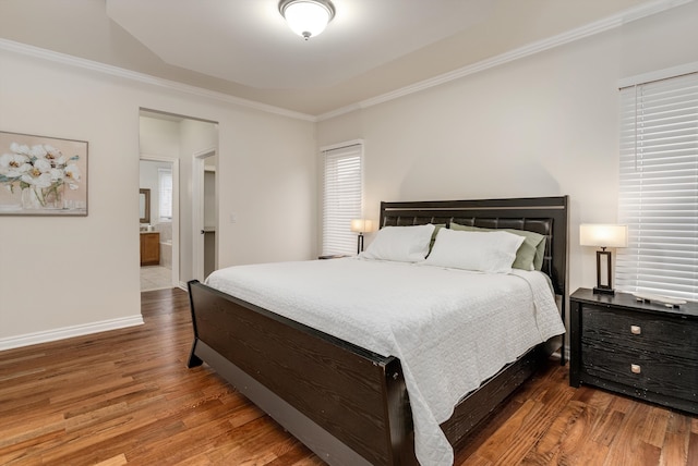 bedroom featuring baseboards, ensuite bath, wood finished floors, and crown molding