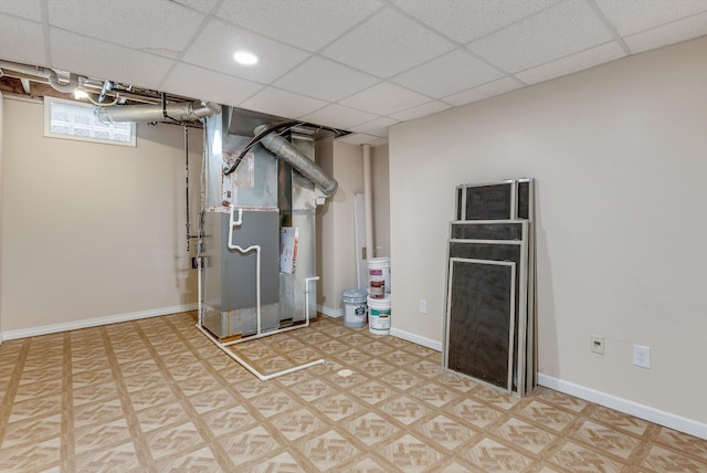 below grade area with a drop ceiling, heating unit, and baseboards