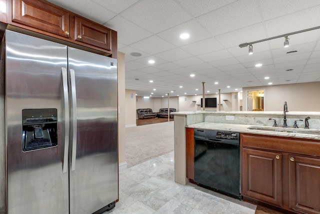 kitchen with light stone counters, a drop ceiling, a sink, black dishwasher, and stainless steel refrigerator with ice dispenser