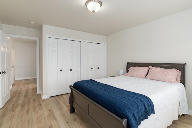 bedroom with two closets, light wood-style flooring, and baseboards