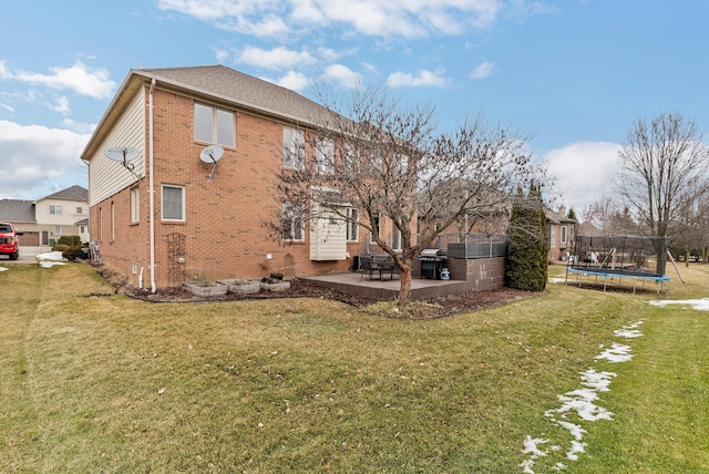 view of side of property featuring a yard, a patio area, a trampoline, and brick siding