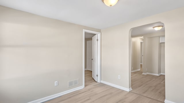 empty room featuring visible vents, baseboards, light wood-style floors, and arched walkways