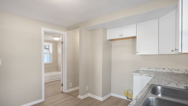 kitchen with a sink, baseboards, light wood-style flooring, and white cabinetry