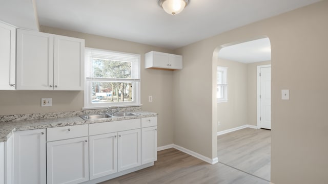 kitchen with a sink, arched walkways, white cabinets, light wood finished floors, and baseboards