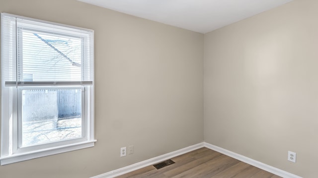 unfurnished room featuring wood finished floors, plenty of natural light, baseboards, and visible vents