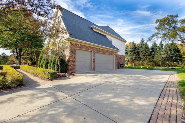 view of home's exterior with a garage, a shingled roof, concrete driveway, and brick siding