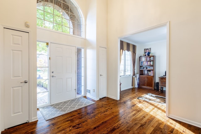 entrance foyer featuring visible vents, baseboards, a towering ceiling, dark wood-style flooring, and crown molding