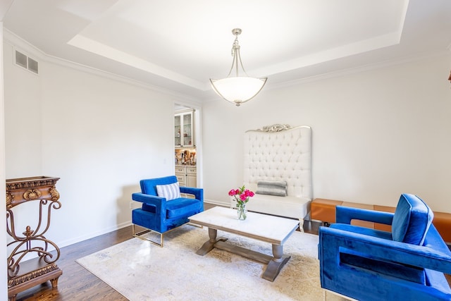 living area featuring crown molding, a raised ceiling, visible vents, wood finished floors, and baseboards