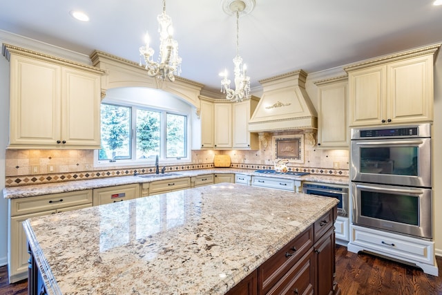 kitchen featuring stainless steel double oven, premium range hood, cream cabinets, and a sink