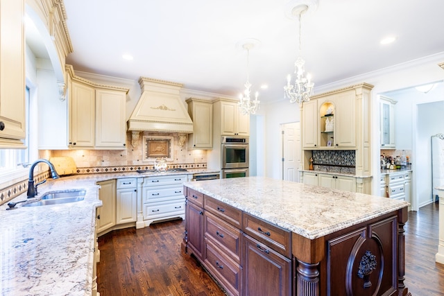 kitchen with light stone counters, cream cabinets, a sink, and custom range hood