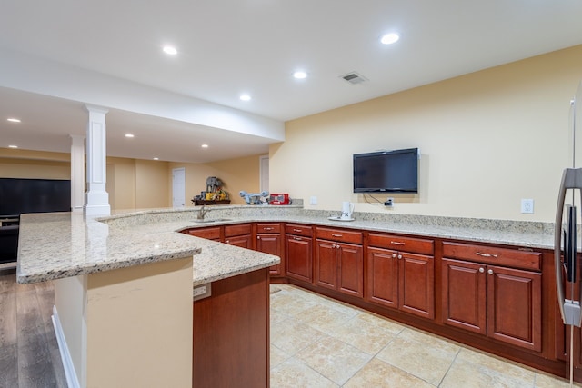 kitchen with decorative columns, visible vents, a sink, light stone countertops, and a peninsula