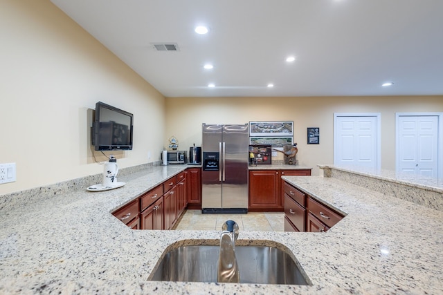 kitchen featuring light stone counters, stainless steel refrigerator with ice dispenser, a sink, and recessed lighting