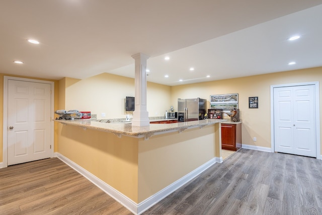 kitchen with light stone counters, a peninsula, light wood-type flooring, stainless steel refrigerator with ice dispenser, and ornate columns