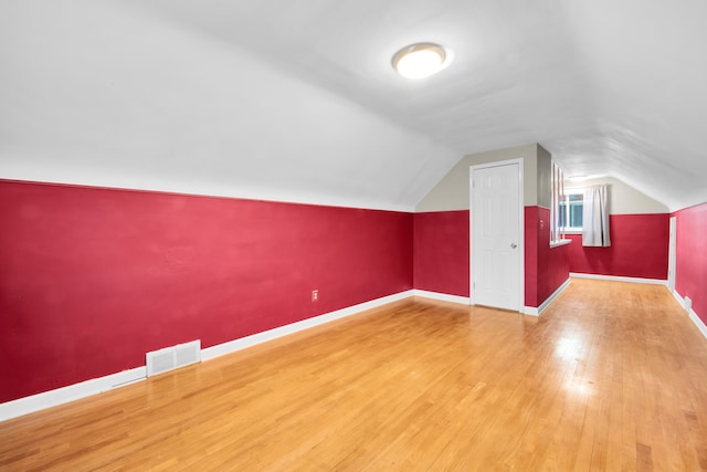 bonus room featuring lofted ceiling, visible vents, baseboards, and wood finished floors