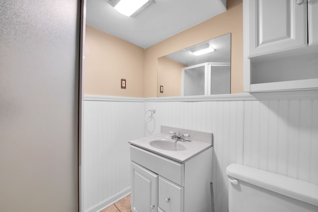 bathroom with toilet, a wainscoted wall, a stall shower, and vanity