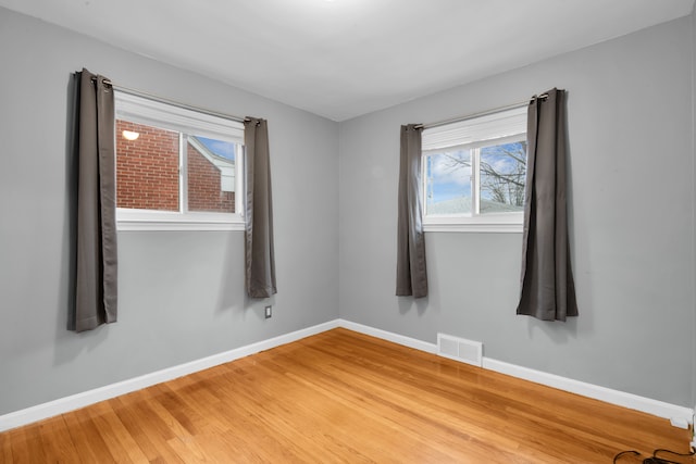 empty room featuring light wood-style flooring, visible vents, and baseboards