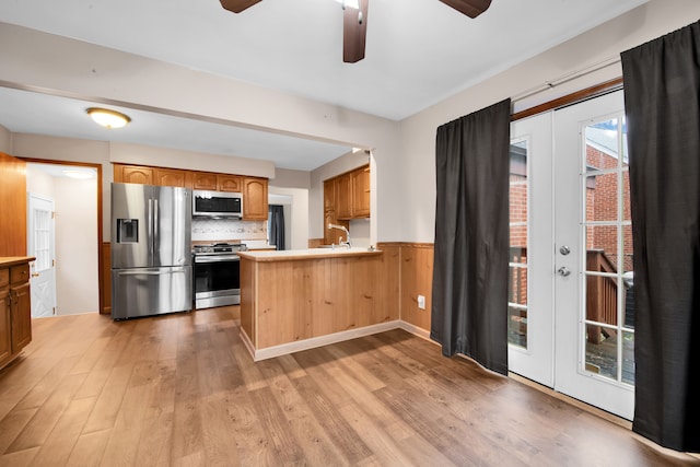 kitchen featuring tasteful backsplash, appliances with stainless steel finishes, a peninsula, light wood-style floors, and a sink