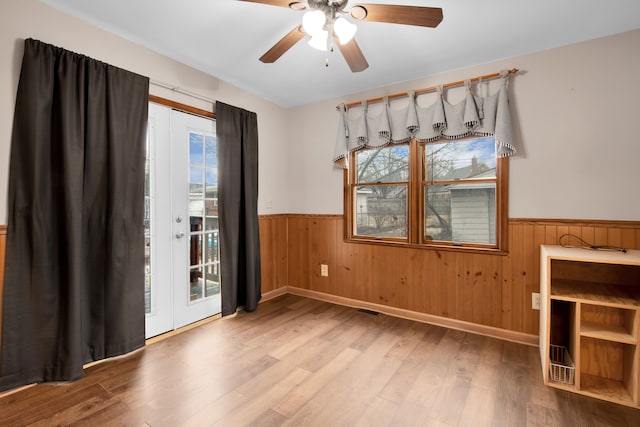 unfurnished dining area featuring a wainscoted wall, wooden walls, a ceiling fan, and wood finished floors