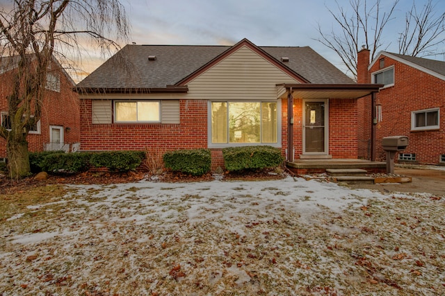 back of house featuring a shingled roof and brick siding