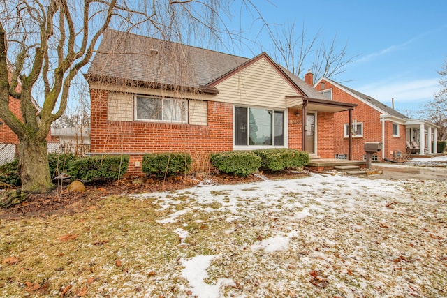 bungalow-style home with roof with shingles, a chimney, and brick siding